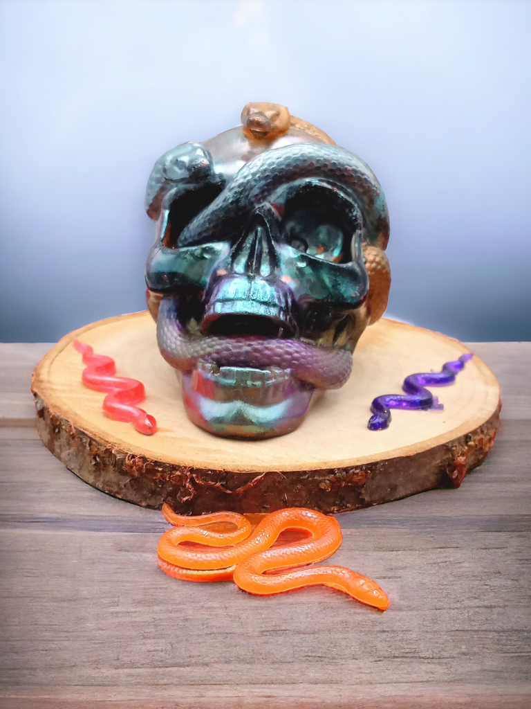 a solid resin skull, in purples and greens wrapped with orange and purple snakes